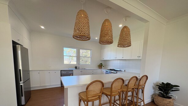A modern kitchen with white cabinets, a large island with bar stools, a refrigerator, and a stove. - The Farmhouse Dunedoo (Dunedoo)