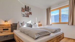 Ein modernes Schlafzimmer mit einem hölzernen Bettgestell, zwei Nachttischen und einem großen Fenster mit Blick auf die Berge.
