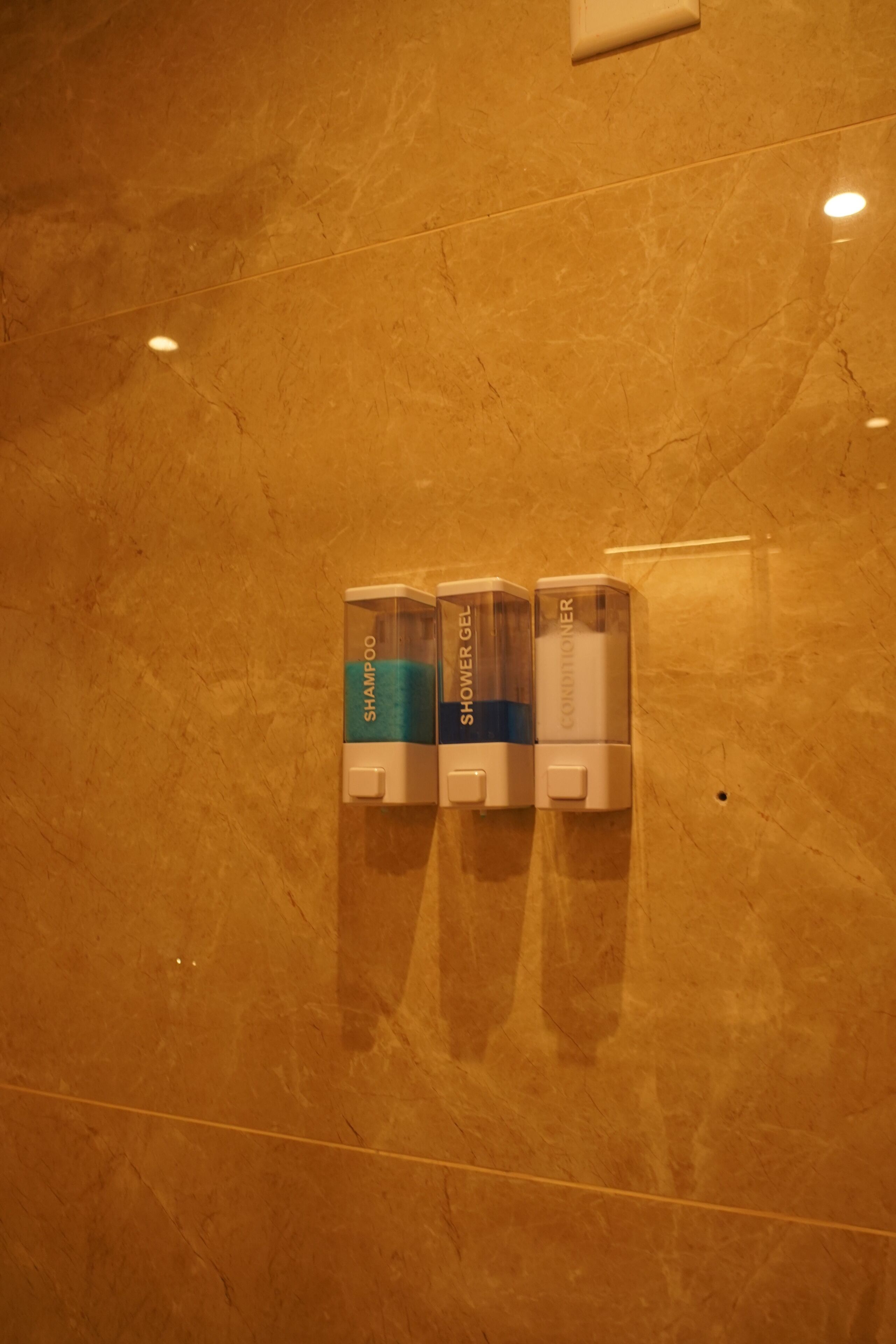 A wall-mounted dispenser with three compartments labeled 'SHAMPOO,' 'SHOWER GEL,' and 'COOLIONER.'