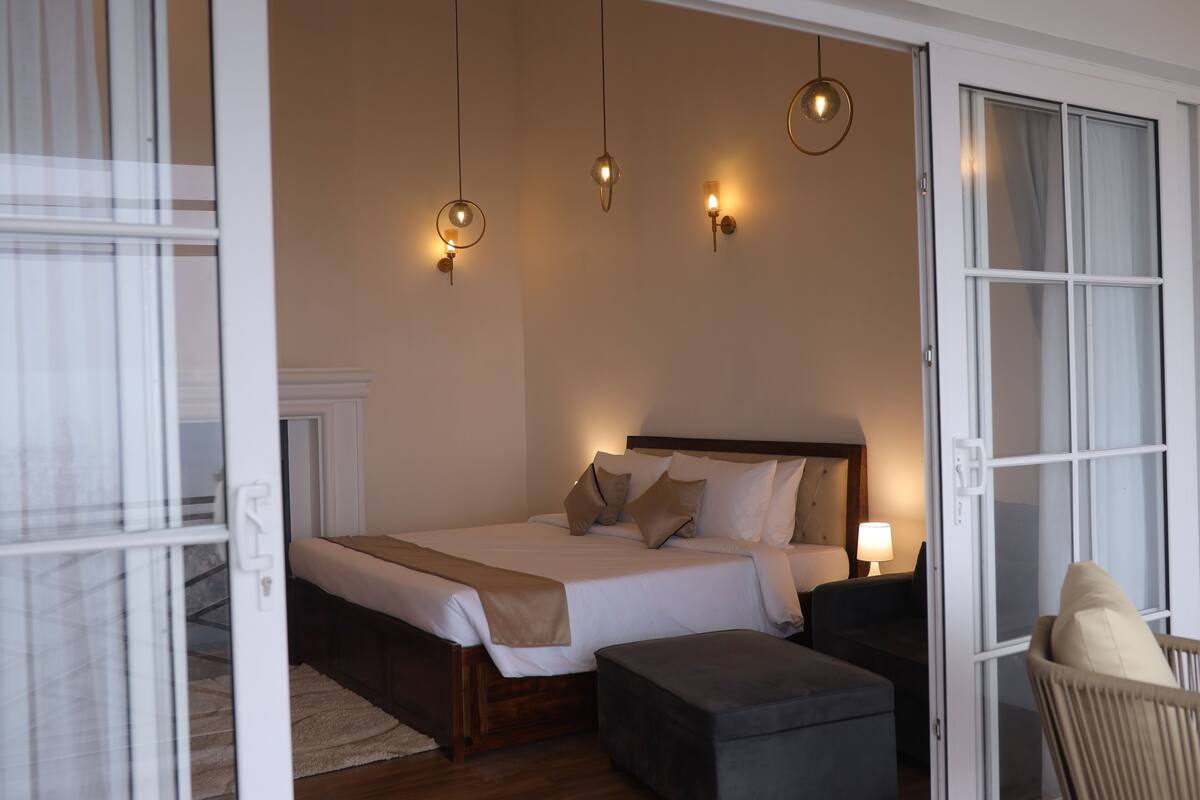 A bedroom with a bed, bedside tables, a chair, and hanging lights.