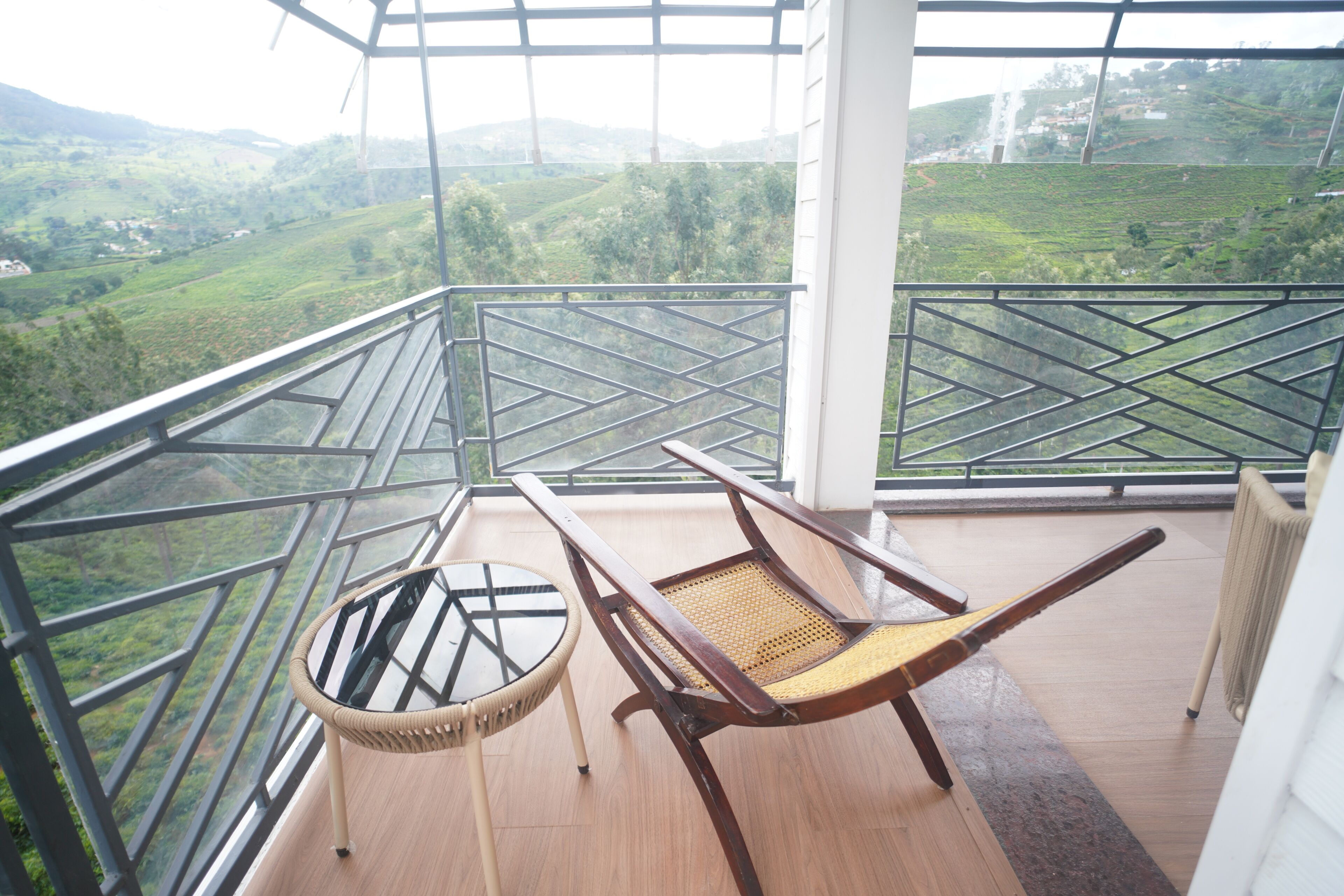 A balcony with a wooden chair and a wicker chair, overlooking a green landscape.