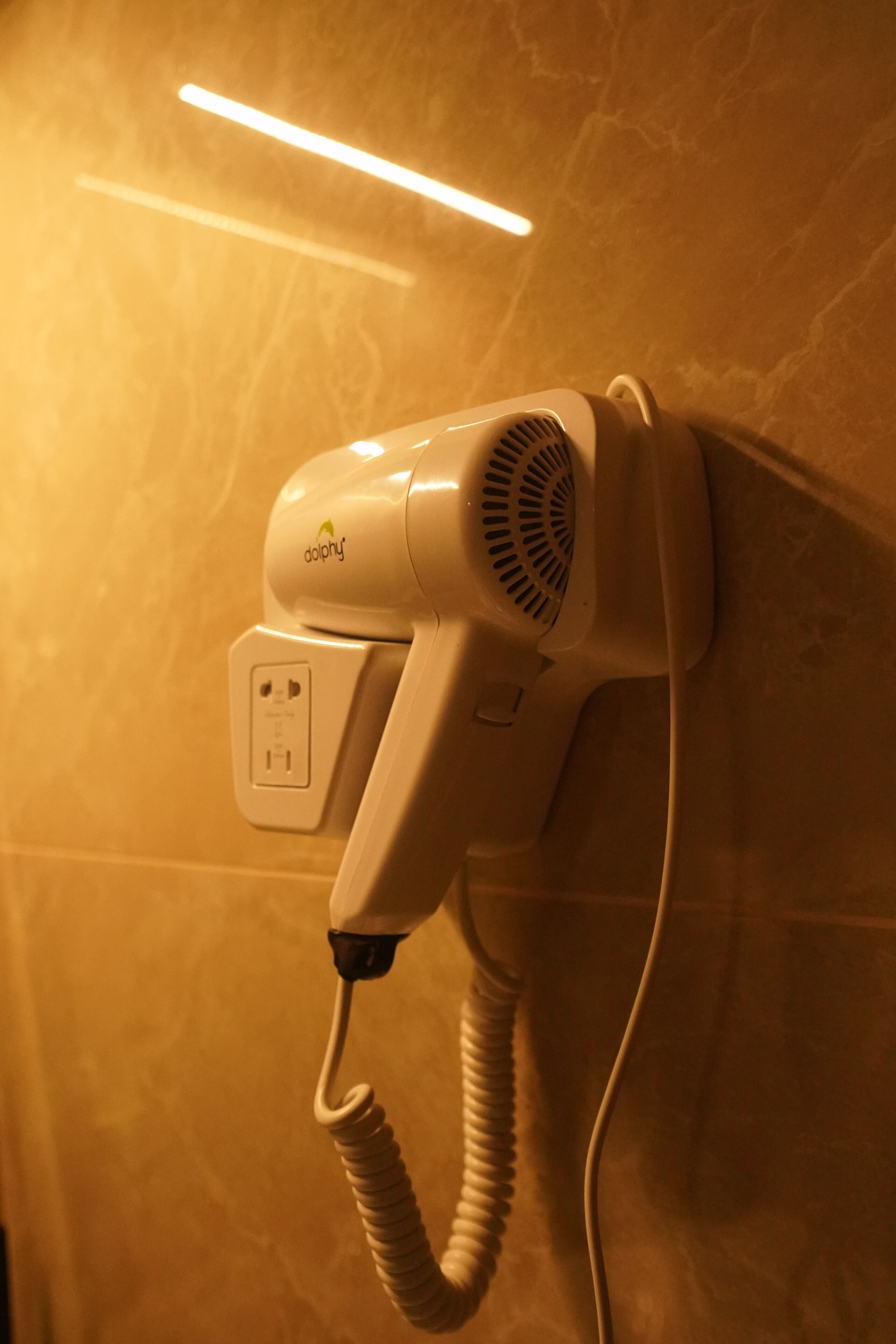A wall-mounted hairdryer with a power cord, connected to a wall socket.