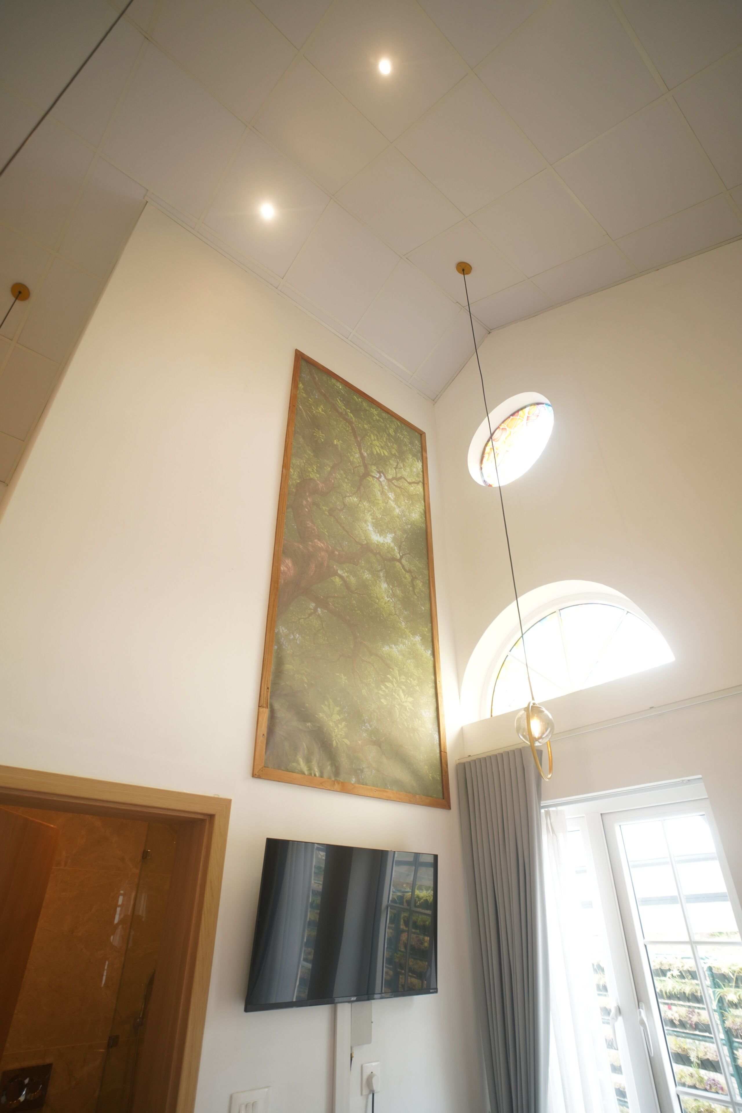 A room with a large painting, a flat-screen TV, and a window with curtains.