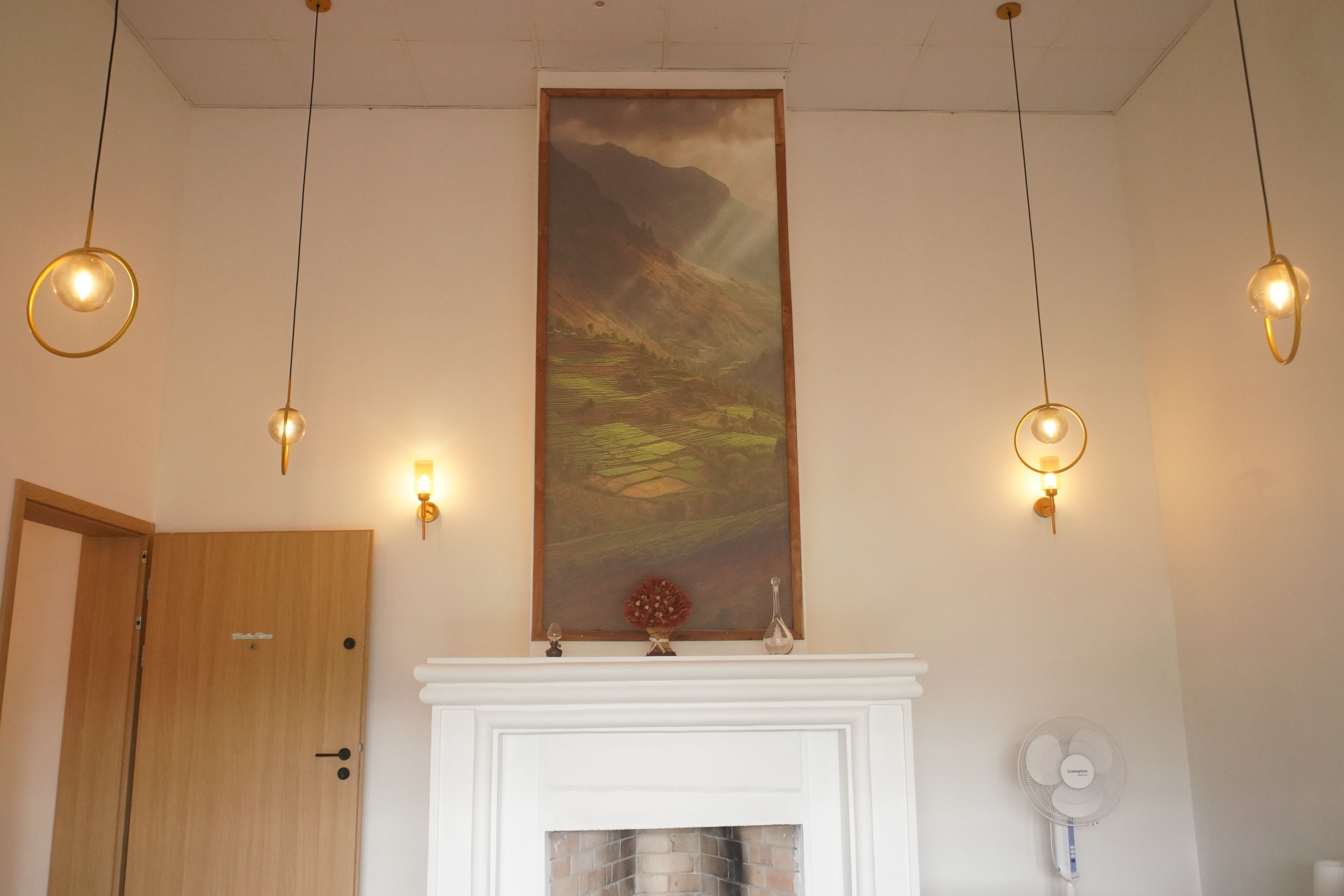 Una habitación con chimenea, un cuadro encima y tres lámparas colgantes.