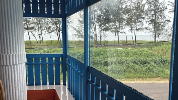 A room with a large window overlooking a grassy area with trees and a body of water. - KUZHUPPILLY BEACH HOUSE (Kochi)