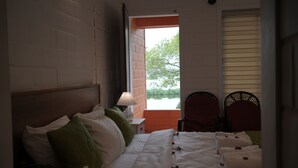 A bedroom with a bed, a nightstand, a lamp, and a window with a view of greenery. - KUZHUPPILLY BEACH HOUSE (Kochi)