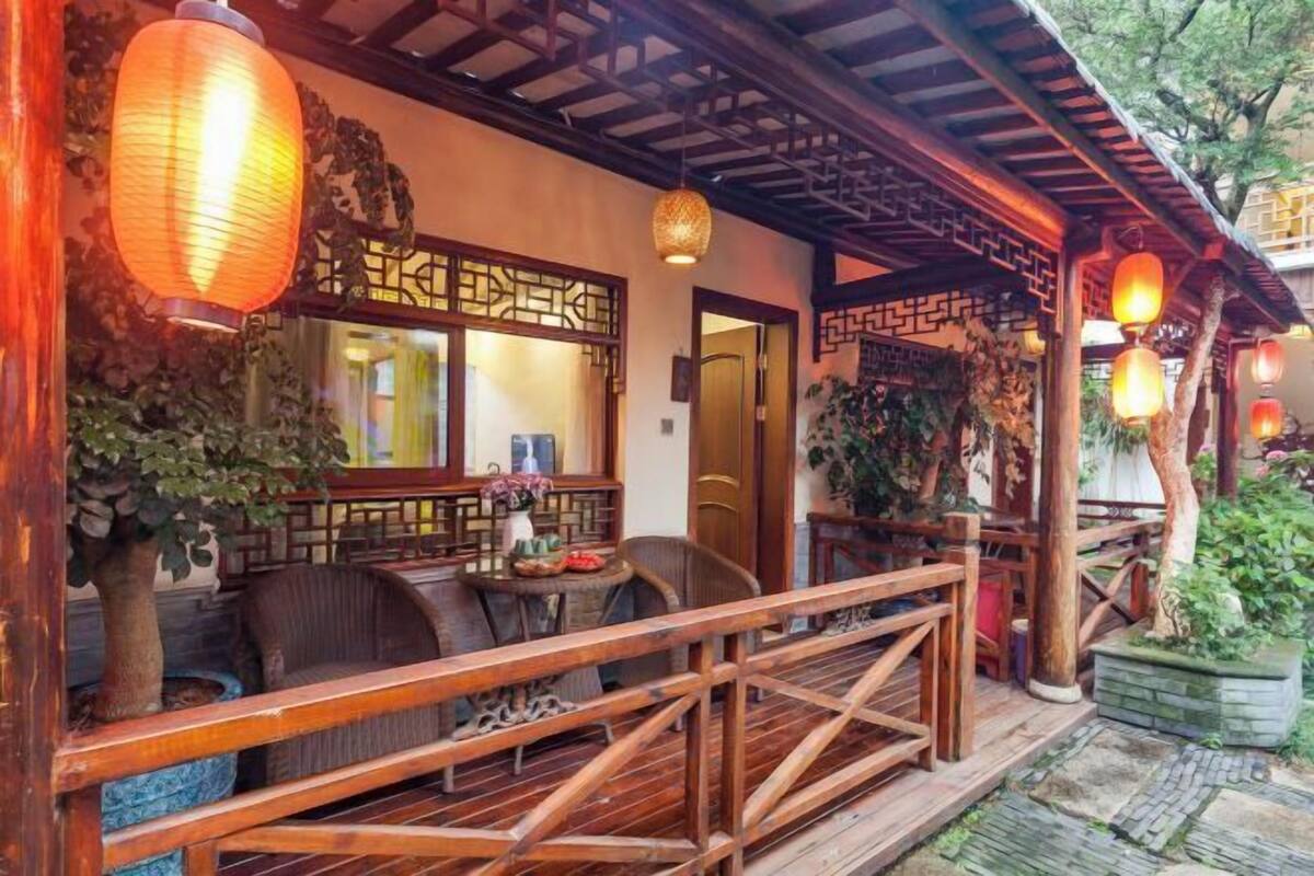 Ein traditionelles Holzgebäude mit überdachter Veranda, einem Essbereich mit Stühlen und Tisch sowie hängenden Laternen.