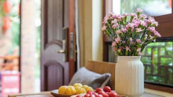 A wooden table with a vase of flowers, a bowl of yellow fruits, and a bowl of red fruits.