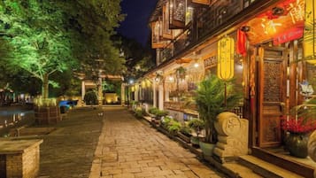 A traditional courtyard with a stone pathway, wooden buildings with lanterns, and potted plants.