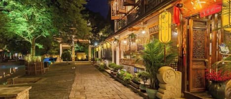 A traditional courtyard with a stone pathway, wooden buildings with lanterns, and potted plants.