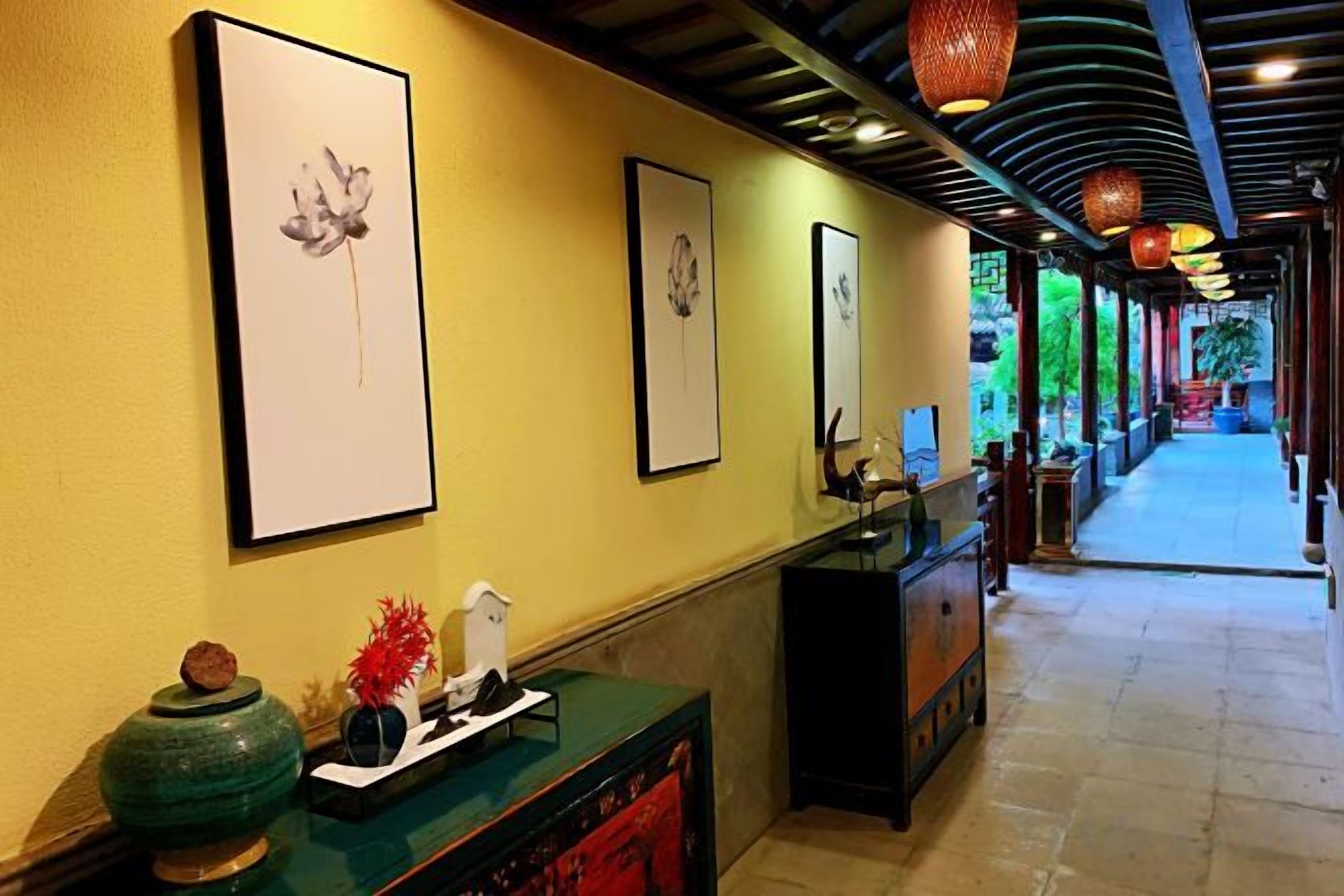 A hallway with framed artwork on the walls, a reception desk, and a decorative vase.