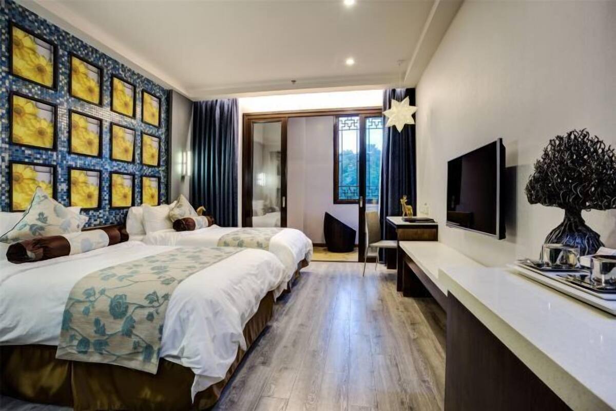 Ein Hotelzimmer mit zwei Betten, einem Fernseher, einem Schreibtisch und einem großen Fenster.