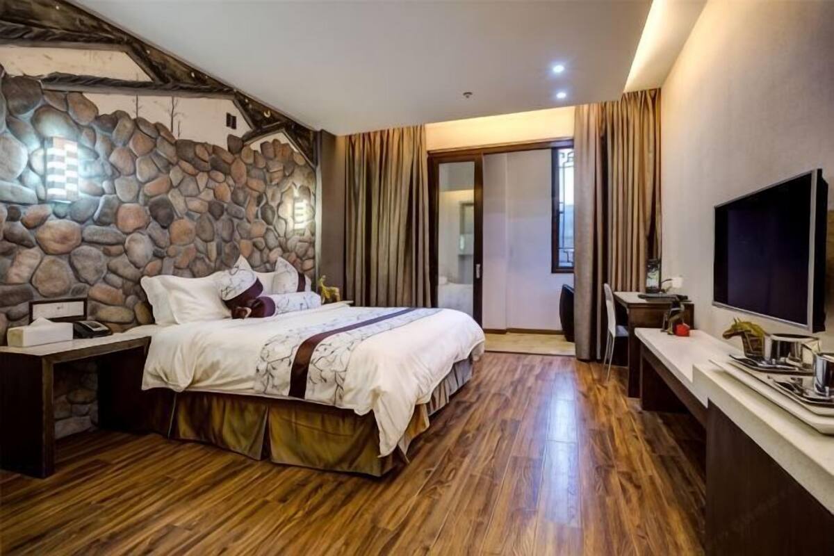 Ein Schlafzimmer mit Steinsandsteinwand, Holzboden, einem Bett mit weißer Bettwäsche, einem Schreibtisch mit Computer und einem Fernseher.
