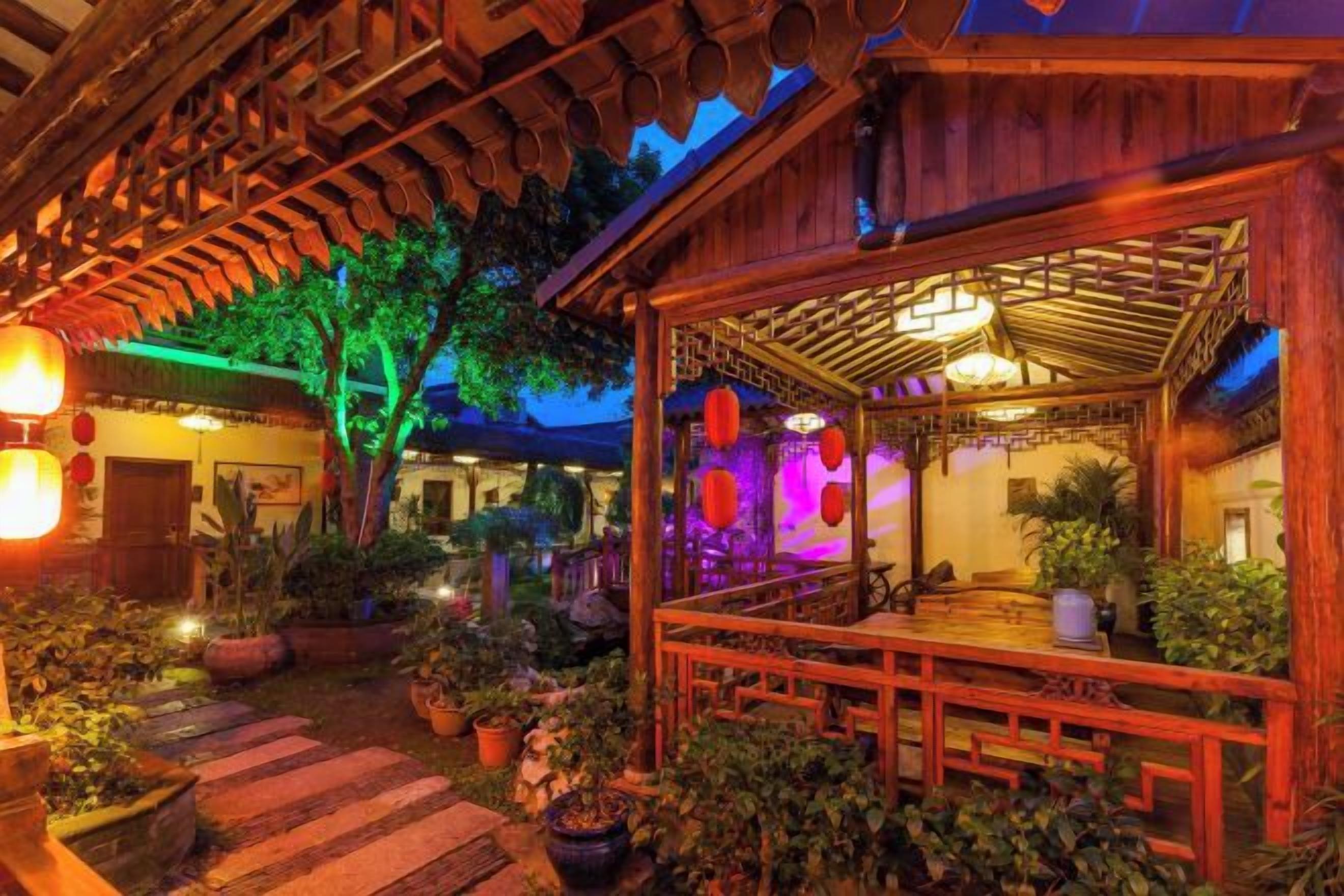 A wooden structure with a covered outdoor seating area, surrounded by potted plants and a stone pathway.