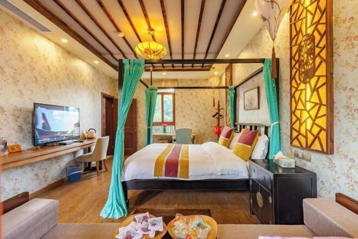 Ein Hotelzimmer mit einem Bett, einem Schreibtisch mit Fernseher, einem Sessel, einer Schreibtischlampe und einem Wandbild.