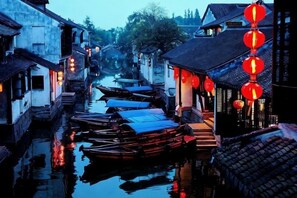 Un canal étroit bordé de bâtiments traditionnels, avec des bateaux amarrés le long des rives et des lanternes rouges suspendues au-dessus.