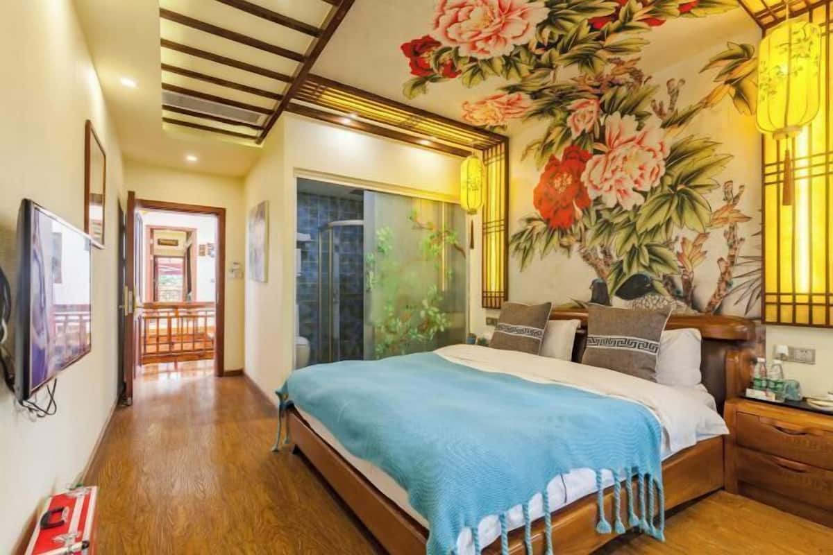 Ein Schlafzimmer mit einem großen Bett, Holzboden, einer Decke mit Gittermuster und einer Wand mit floralem Wandbild.