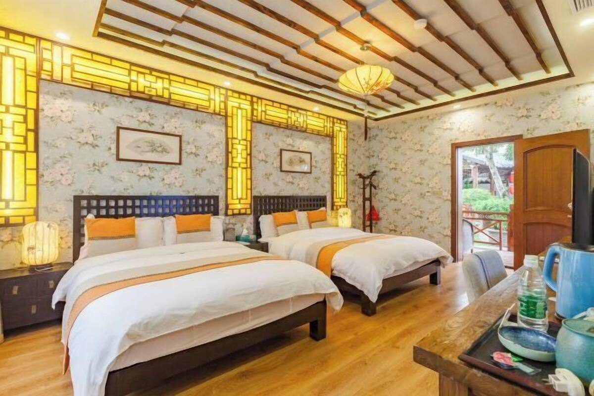 Ein Zimmer mit zwei Betten, Holzboden, Deckenbalken und einer Wand mit floralem Muster.