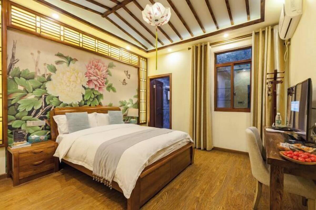 Ein Schlafzimmer mit Bett, Nachttisch, Schreibtisch, Stuhl und einer großen Wandmalerei mit floralem Muster.
