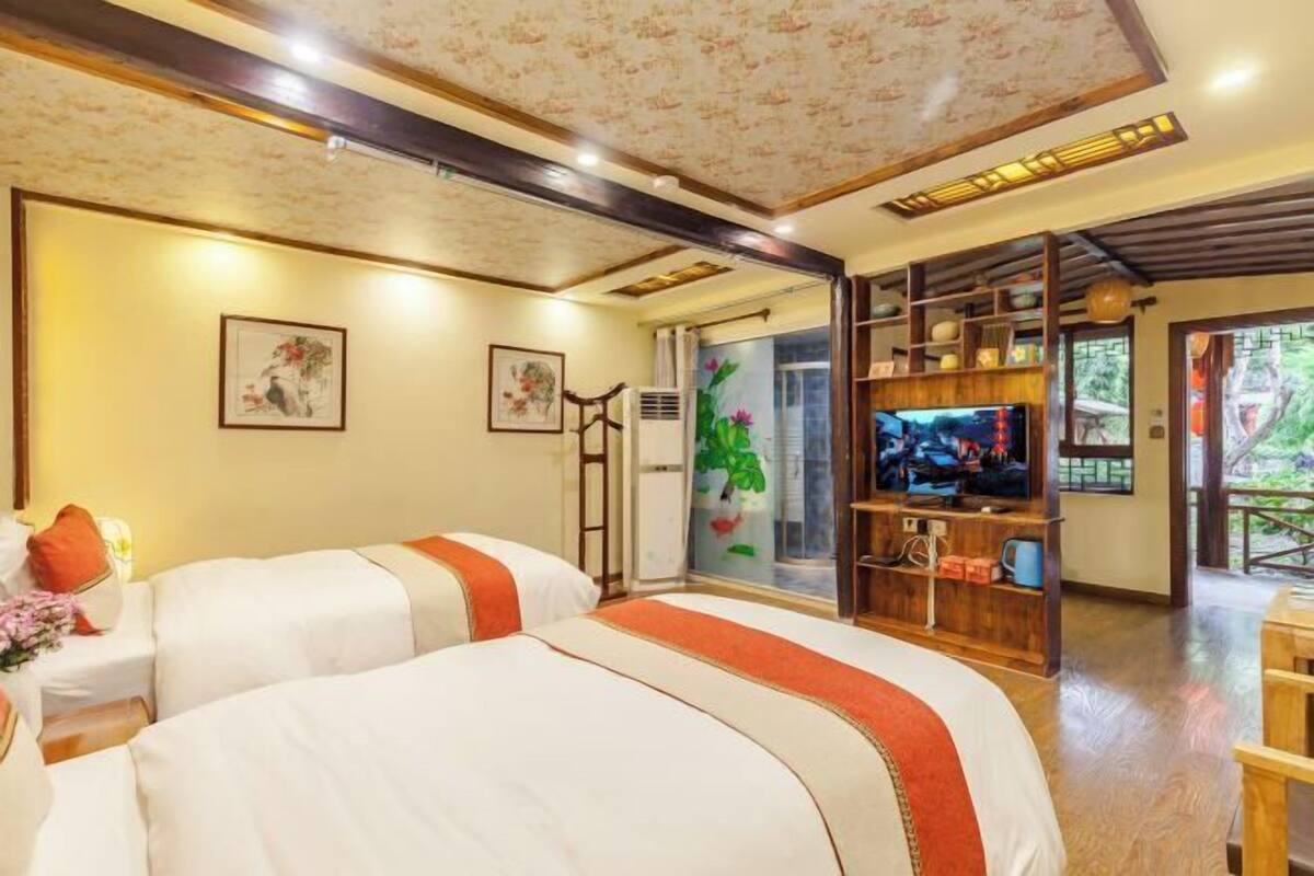 Ein Hotelzimmer mit zwei Betten, einem Fernseher, einem Holzregal und Blick ins Freie.