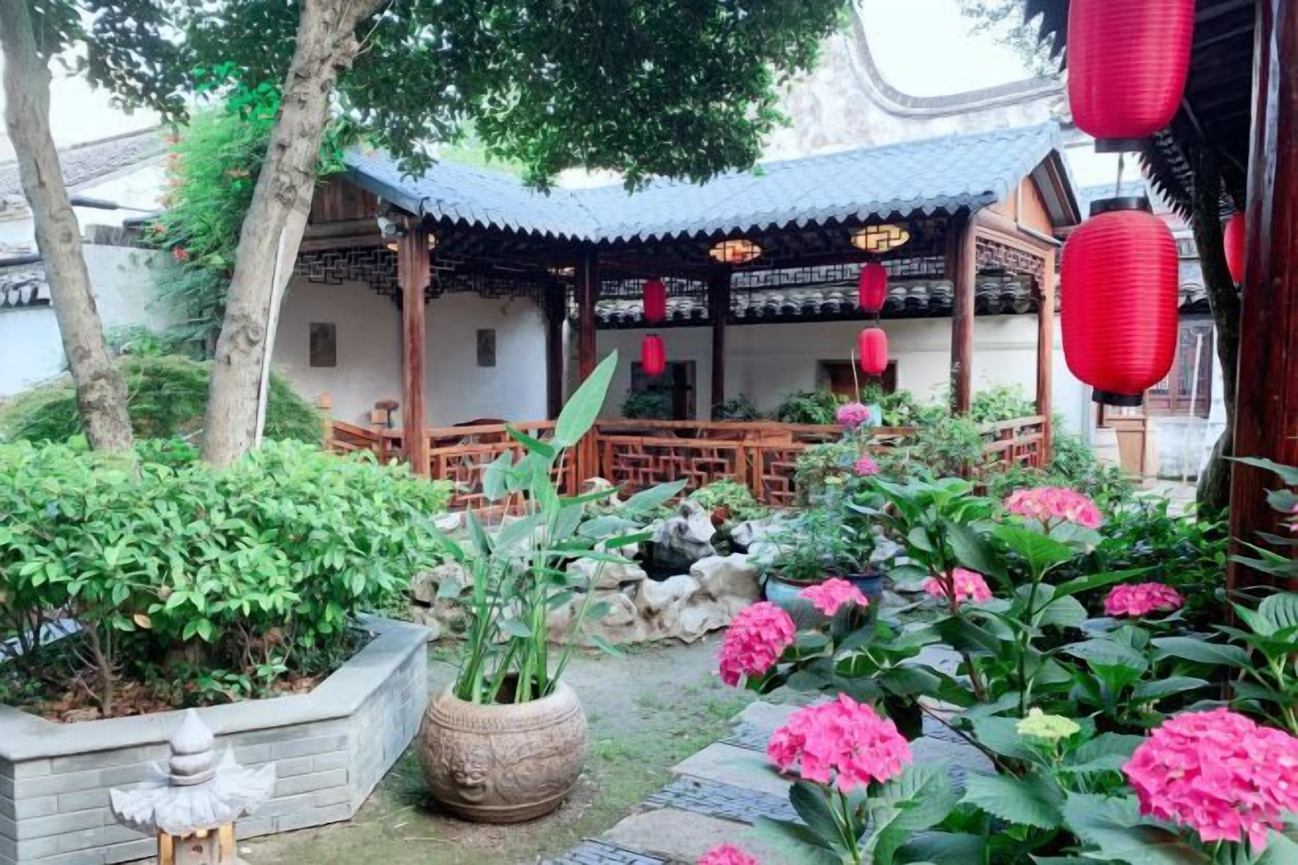 A traditional courtyard with a wooden pavilion, stone lanterns, and potted plants.