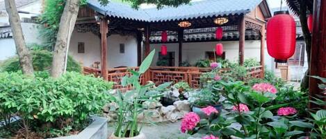 A traditional courtyard with a wooden pavilion, stone lanterns, and potted plants.