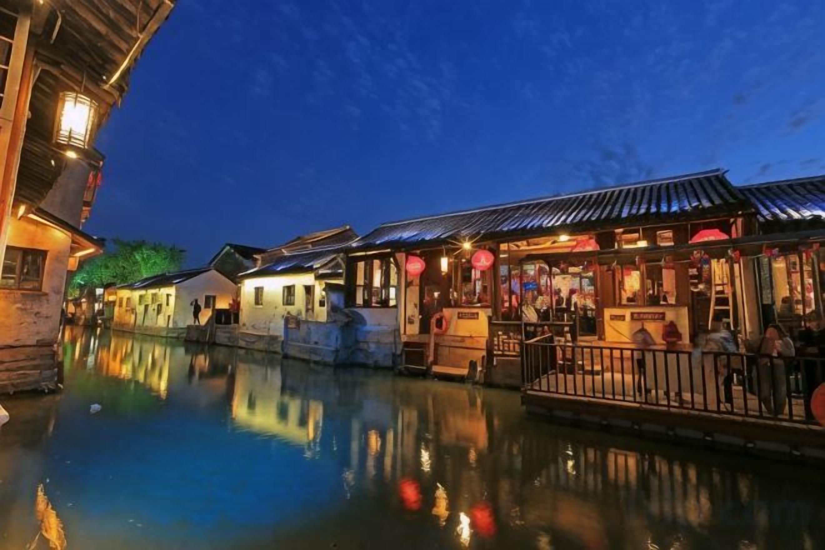 A riverside scene with traditional buildings, a wooden walkway, and a calm water body reflecting the structures.