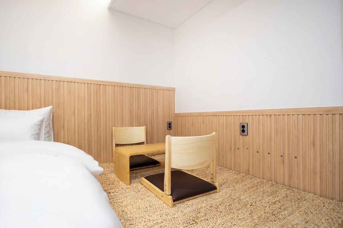 Una habitación con una cama, un banco de madera y una silla con cojín.