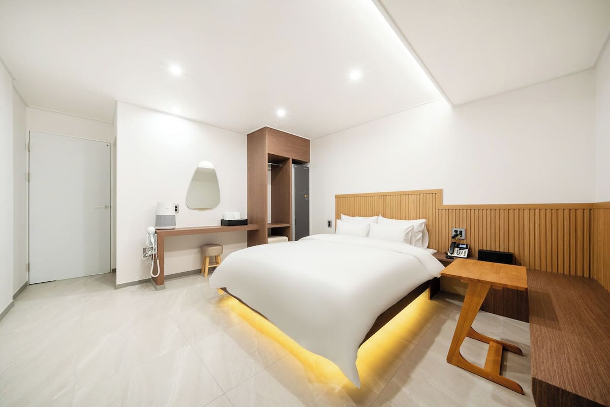 Una habitación de hotel moderna con una cama grande, mesita de noche, escritorio y armario.