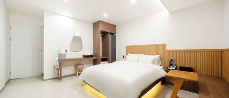 Una habitación de hotel moderna con una cama grande, mesita de noche, escritorio y armario.