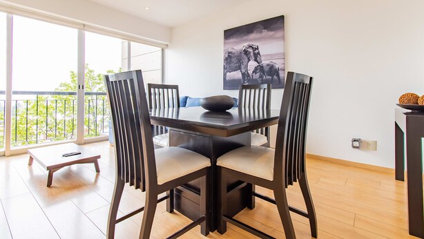 A dining area with a table and chairs, a painting on the wall, and a balcony with a view. - City Views Santa Fe I Lovely 1 BR Apartment Within Santa Fe (Mexico City)