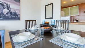 A dining area with a dark wooden table set for four, surrounded by chairs. There is a large framed picture on the wall, a bowl of fruit on the table, and a glass of water. - City Views Santa Fe I Lovely 1 BR Apartment Within Santa Fe (Mexico City)