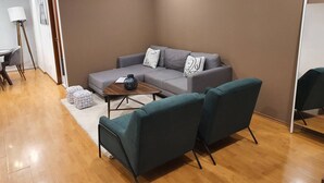 Een moderne woonkamer met een grijze bank, blauwgroene fauteuils en een houten salontafel.