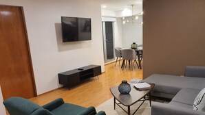 Een moderne woonkamer met een flatscreen televisie, een bank, een salontafel en een eethoek met stoelen en een tafel.