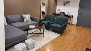 Een moderne woonkamer met een grijze bank, teal fauteuils, een salontafel en een klein wit vloerkleed.