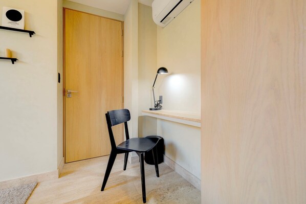 A room with a wooden door, a black chair, a desk with a lamp, and a shelf with a small item. - Aristoteles Elegance Comfort 1 BR Apartment wit (Mexico City)