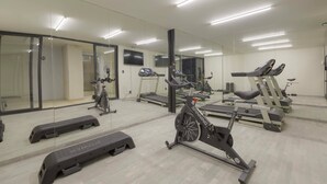 Un gimnasio con cintas de correr, bicicletas estáticas y un espejo grande.
