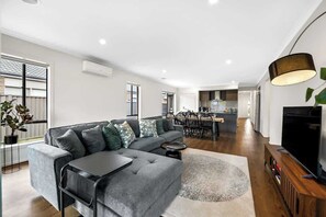 Ein modernes Wohnzimmer mit einem grauen Ecksofa, einem kleinen runden Couchtisch und einem Flachbildfernseher auf einem Holzgestell.