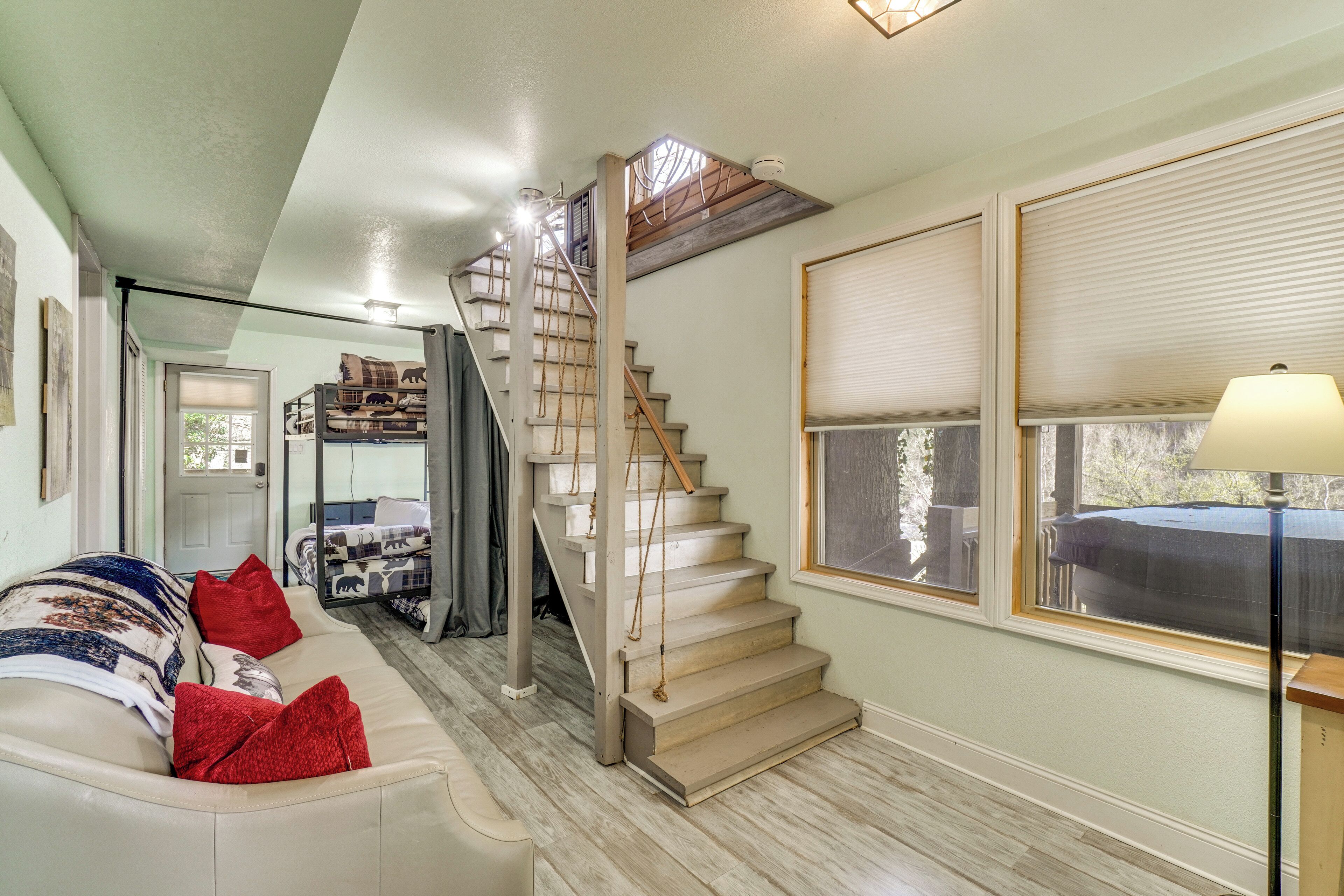Un escalier menant à une chambre à coucher située en mezzanine, un canapé avec des coussins rouges et une lampe près d’une fenêtre.
