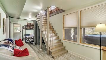 Un escalier menant à une chambre à coucher située en mezzanine, un canapé avec des coussins rouges et une lampe près d’une fenêtre.