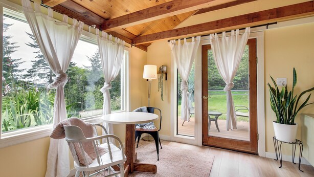 Una habitación con techo de madera, una mesa redonda con sillas, una planta en maceta y vistas al exterior con vegetación.