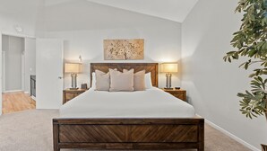 Une chambre à coucher avec un lit en bois, deux tables de chevet avec des lampes, une œuvre d’art accrochée au mur et une plante.