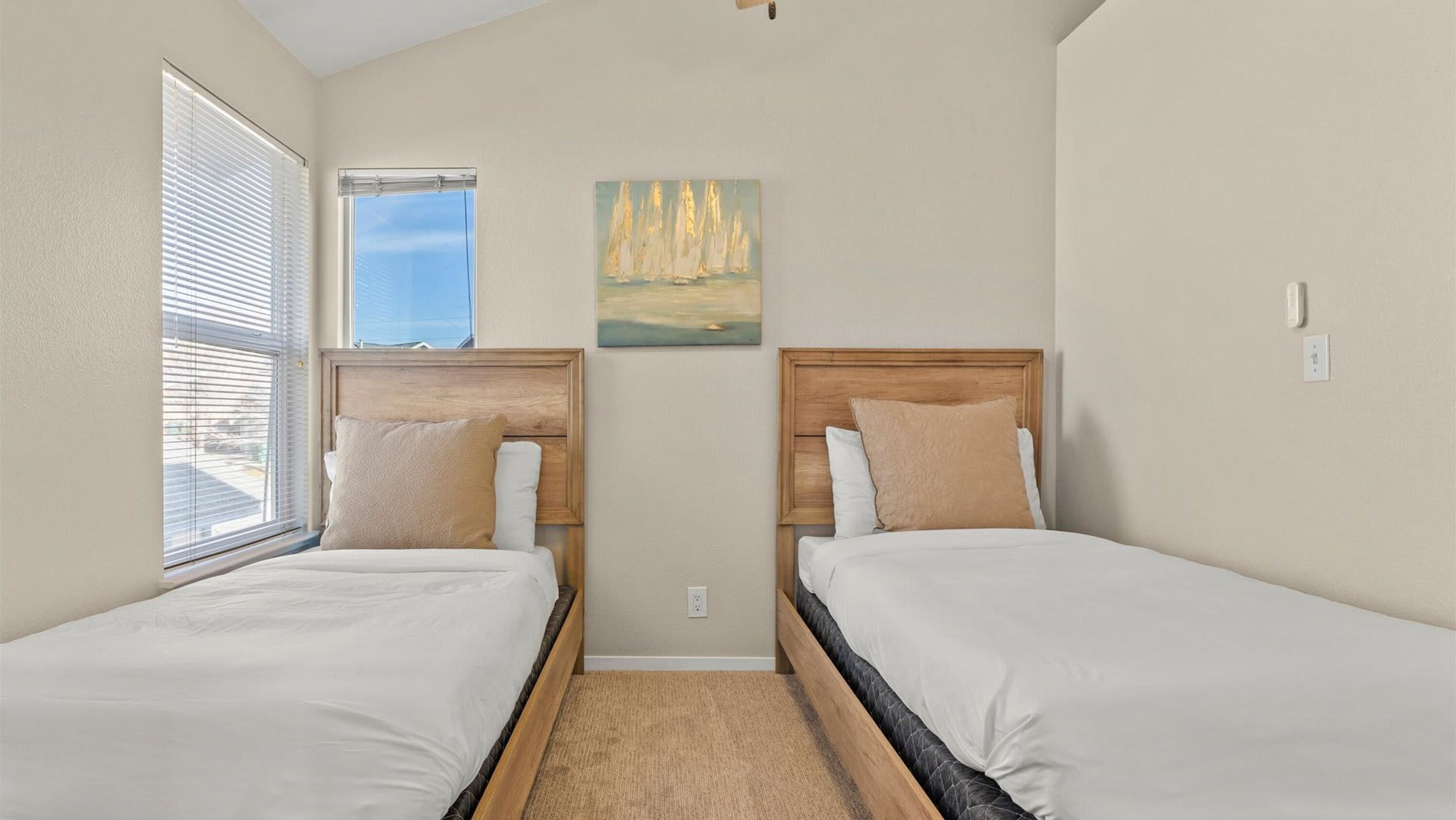 A bedroom with two beds, a painting on the wall, and a window with blinds.