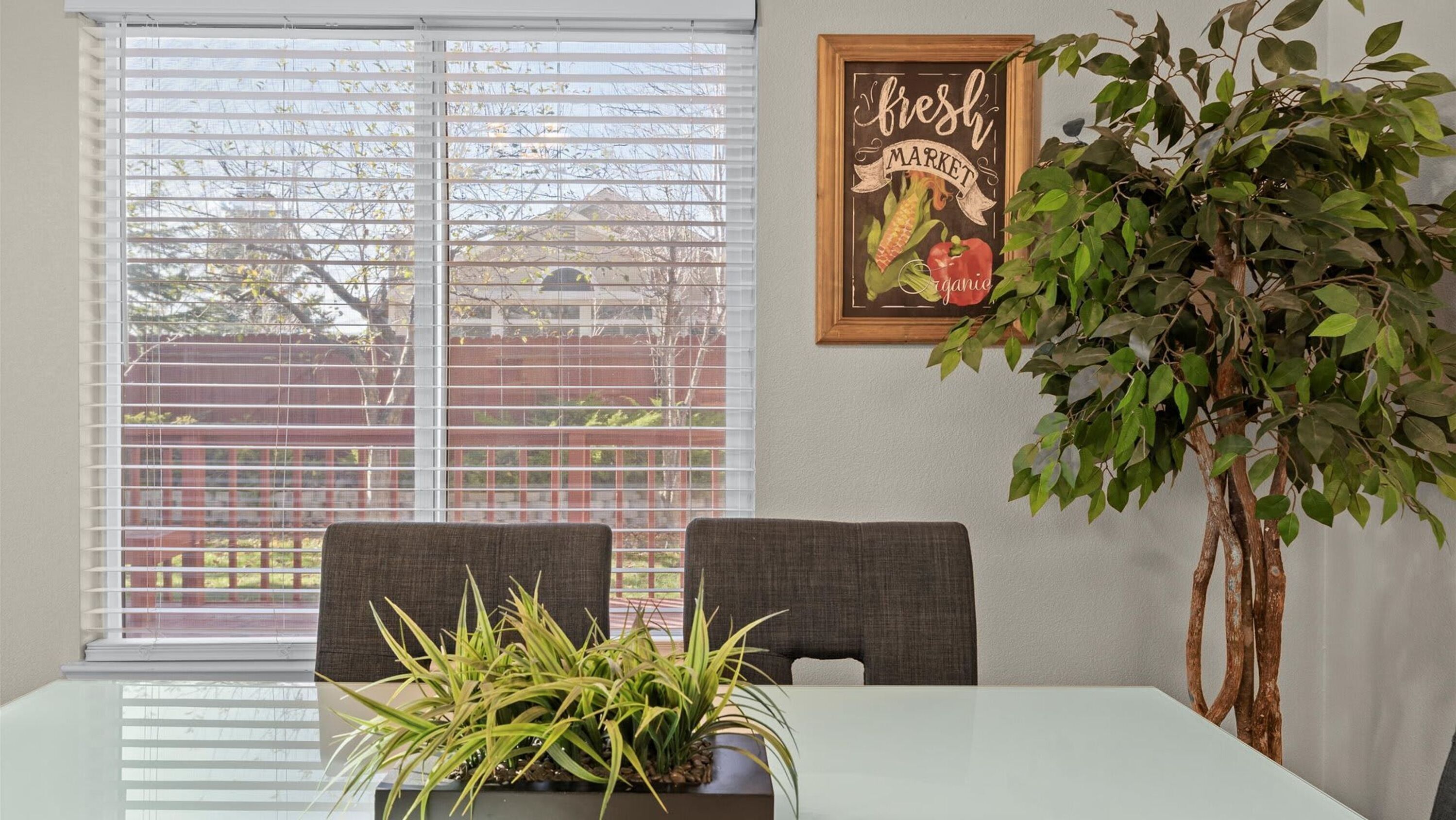 A dining area with a table, two chairs, a potted plant, and a wall-mounted sign.