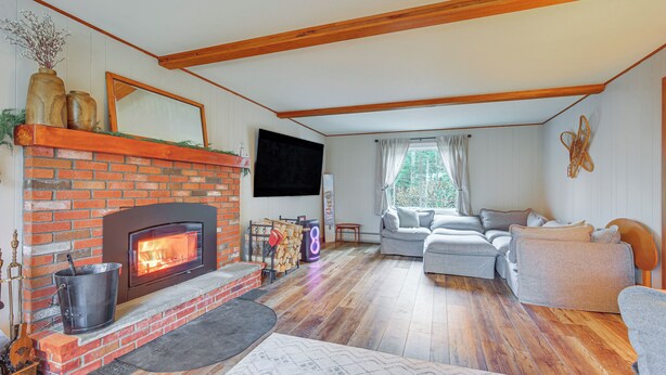 Una sala de estar con chimenea de ladrillo, un televisor de pantalla plana montado encima, un sofá gris y techo de madera.