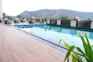 A rooftop pool with a view of mountains, surrounded by chairs and potted plants. - Pride Premier Alwar, Sariska  (Alwar)