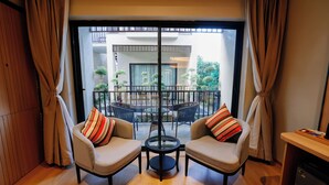 A room with two sofas, a small table, and a view of an outdoor balcony with plants and a dining area. - Pride Premier Alwar, Sariska  (Alwar)