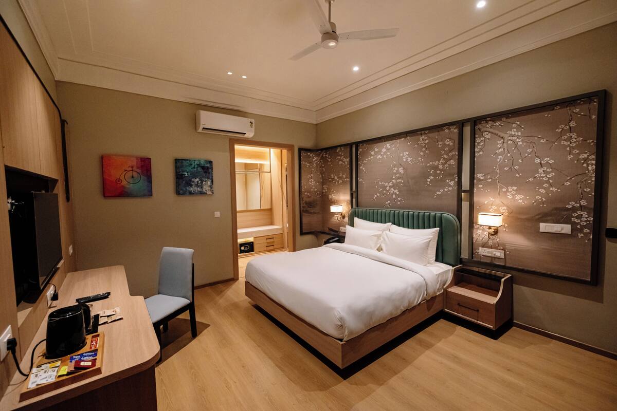 Une chambre d’hôtel comprenant un lit, des tables de chevet, un bureau avec une chaise, une télévision et des œuvres d’art accrochées aux murs.