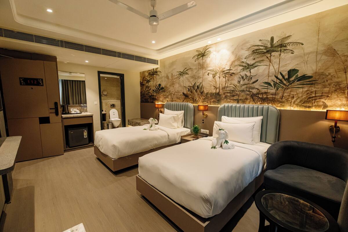 Une chambre d’hôtel avec deux lits, un bureau, une chaise, un minibar et une fresque représentant des plantes tropicales sur le mur.