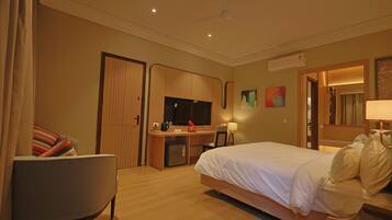 Quarto de hotel com cama, escrivaninha, cadeira, televisão e um pequeno frigorífico.